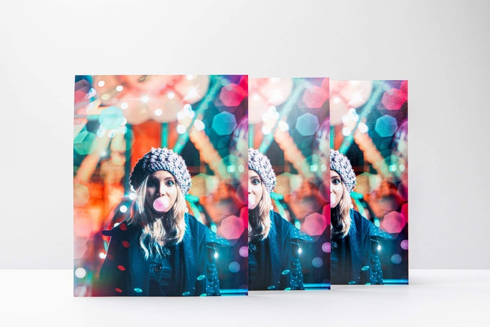 Three prints of a girl with a knit hat blowing bubblegum in front of an out of focus ferris wheel creating colorful bokeh, comparing deep matte and lustre coating