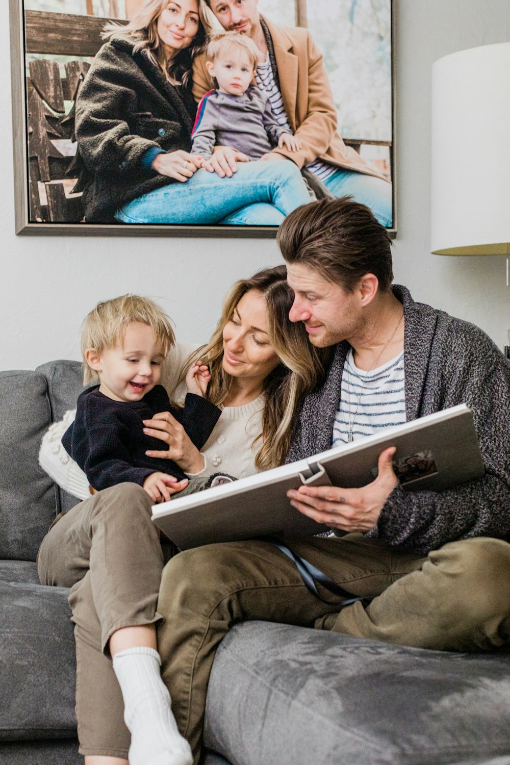 A family sitting on a couch looking at a photo album.