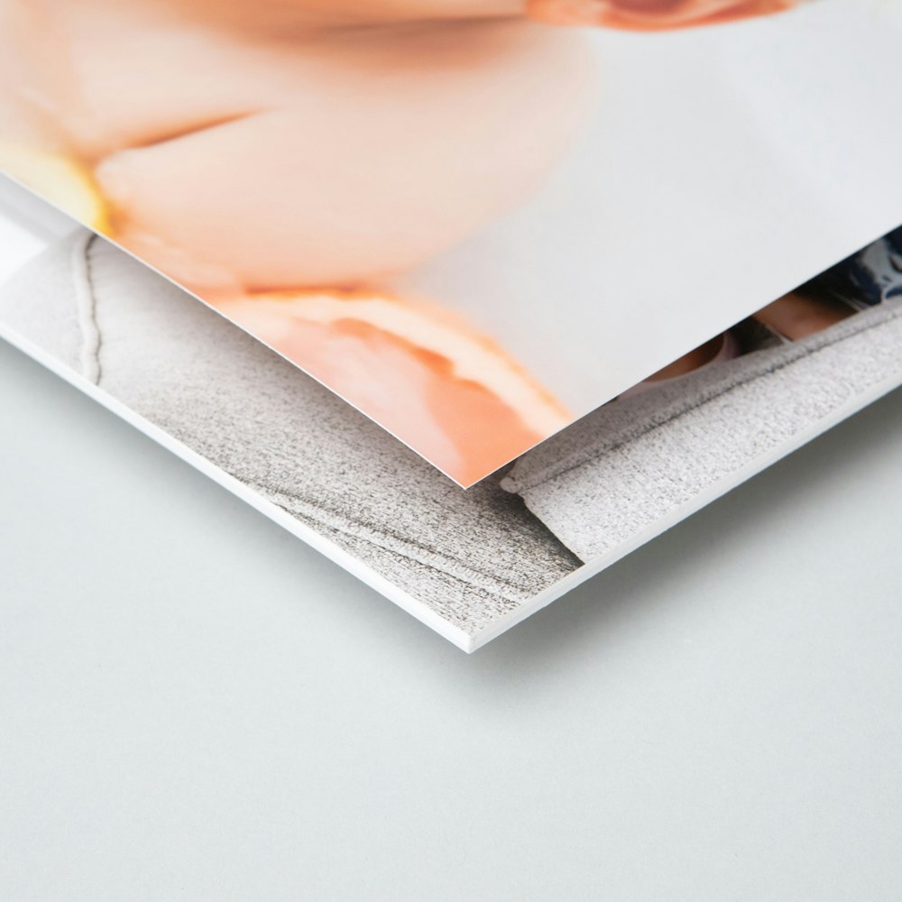 A close-up of two photo print corners with the top one showing a partial image of a baby's face with a soft, warm tone against a textured gray background.