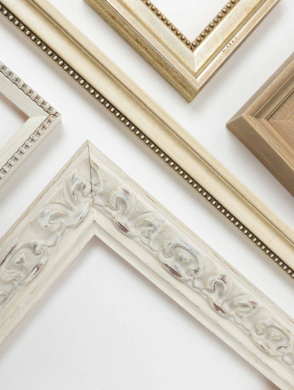 Four empty picture frames and sample corners with white, gold, and ivory finishes are arranged on a white background.