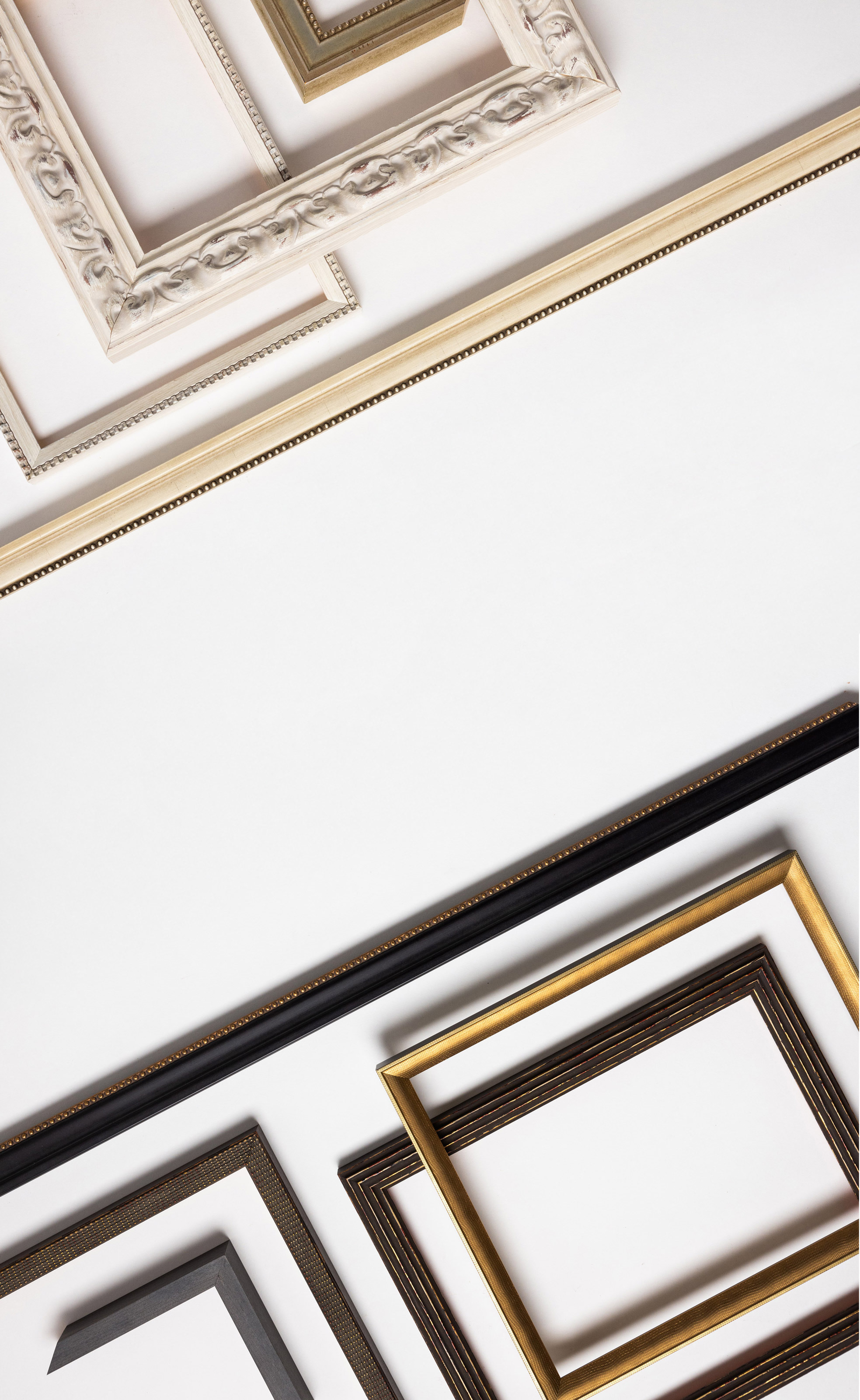 Flatlay of various black, dark brown, gold, ivory, and white Framed Print mouldings arranged into a pattern from light to dark
