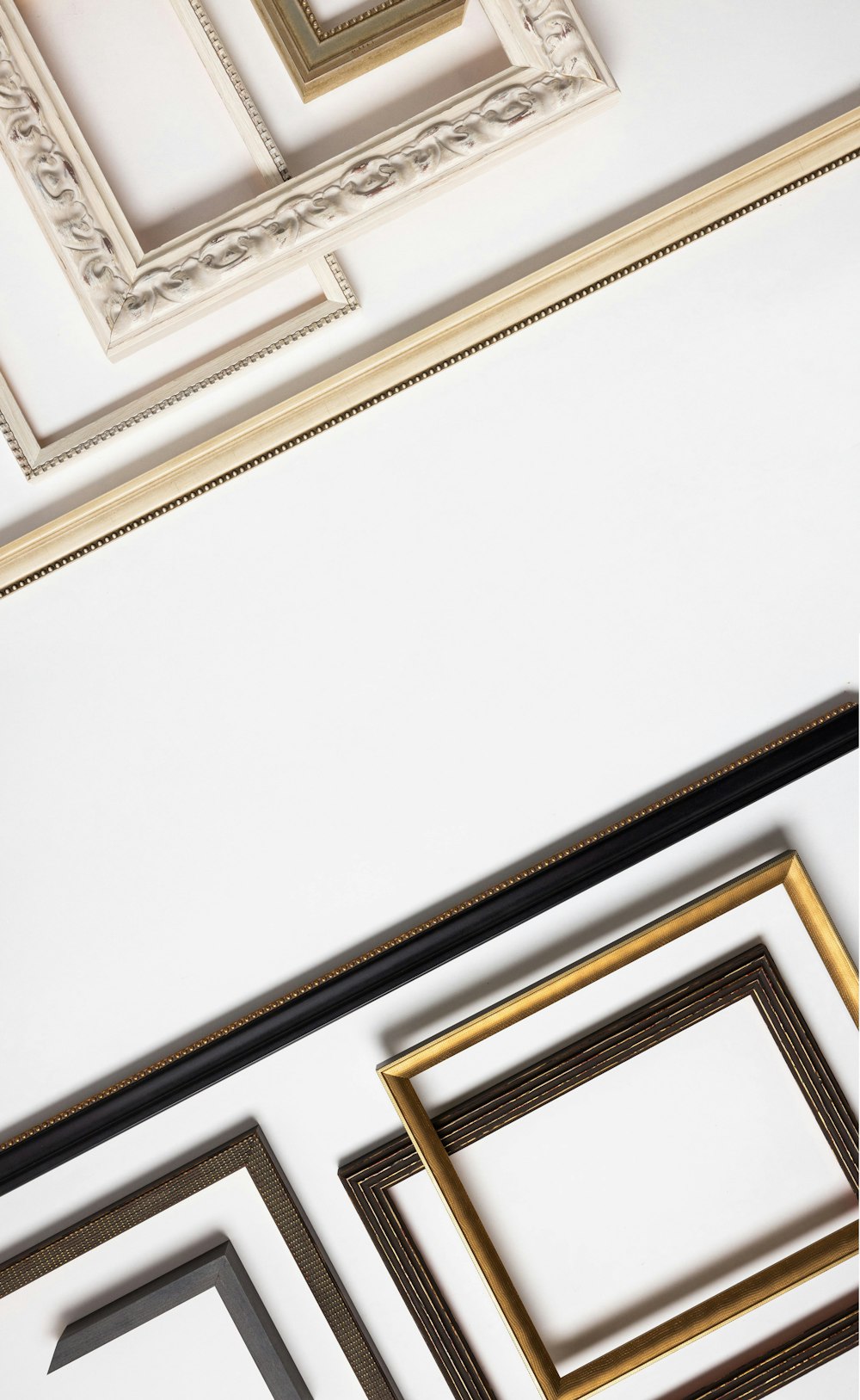 Flatlay of various black, dark brown, gold, ivory, and white Framed Print mouldings arranged into a pattern from light to dark
