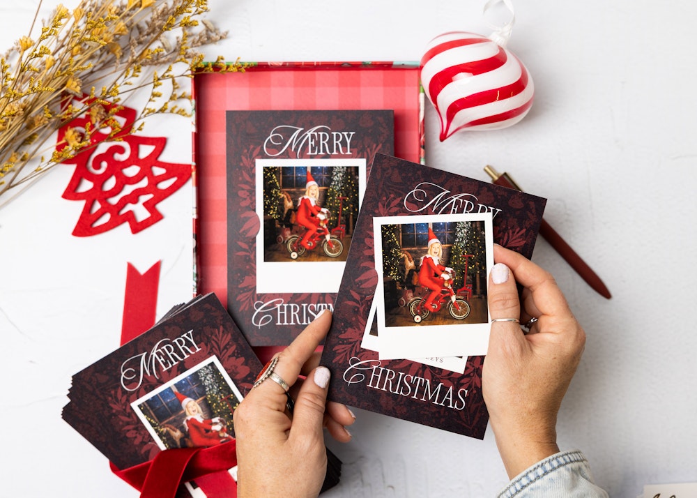 Hand inserting a Mini Snapshot print of an image from a child's santa themed photo session into curved slots in a red "Merry Christmas" holiday Flat Card to hold the print to it.