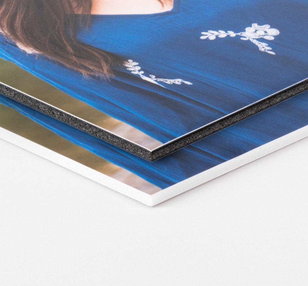 Two stacked photo prints of a person wearing a blue top with white floral embroidery, with the top print mounted on black foam board and the bottom one mounted on white foam board.