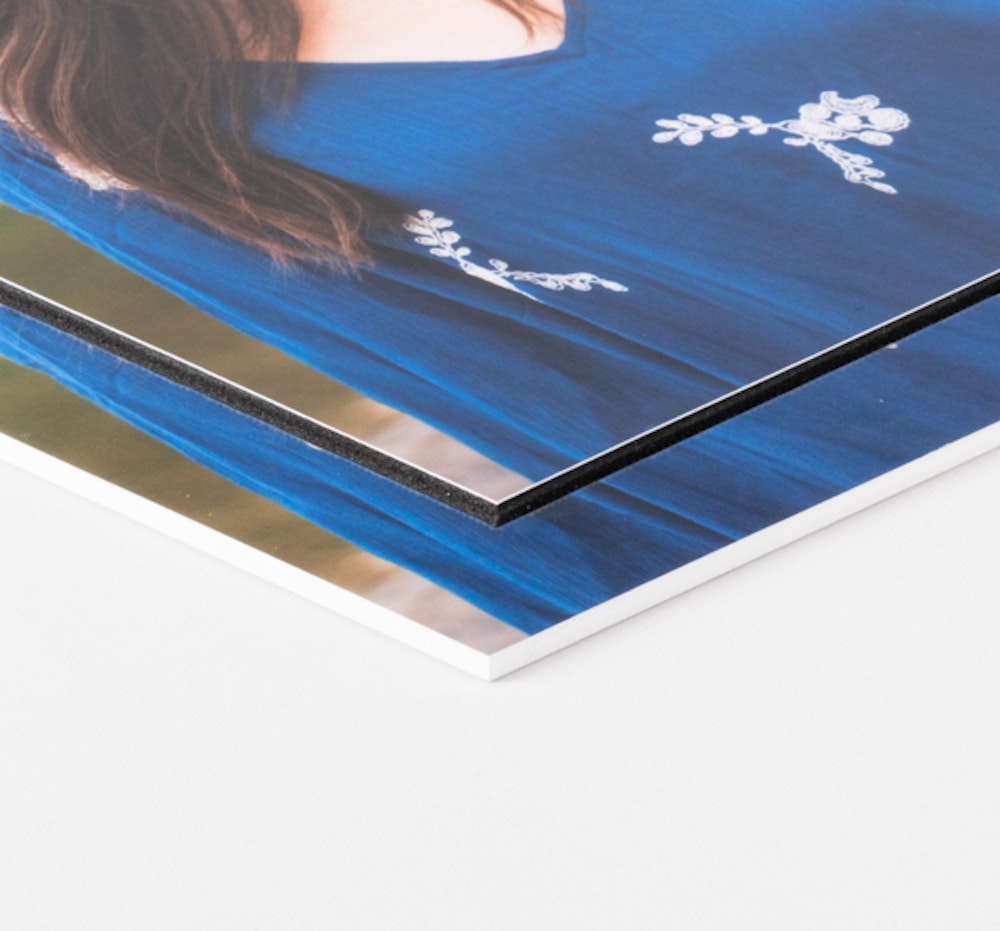 Two stacked photo prints of a person wearing a blue top with white floral embroidery, with the top print mounted on black styrene and the bottom one mounted on white styrene.