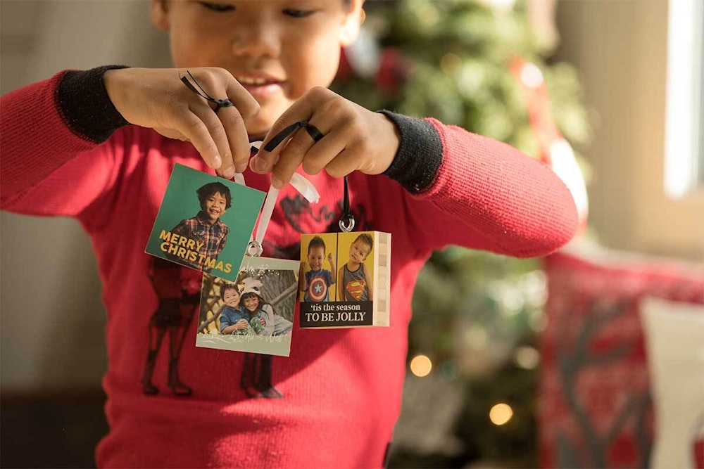 Kid holding multiple Bamboo Ornaments with holiday designs in front of Christmas tree