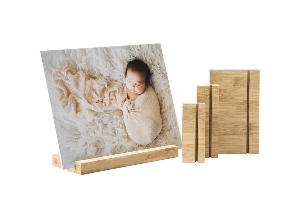 A newborn baby wrapped in a soft blanket is displayed on a wood display stand alongside additional wood display stands.