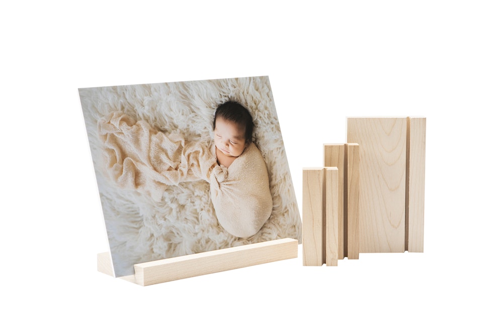 A newborn baby wrapped in a soft blanket is displayed on a wood display stand alongside additional wood display stands.