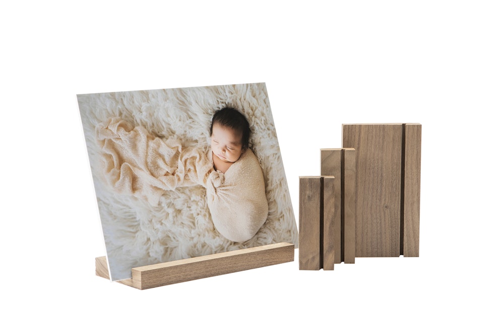 A newborn baby wrapped in a soft blanket is displayed on a wood display stand alongside additional wood display stands.