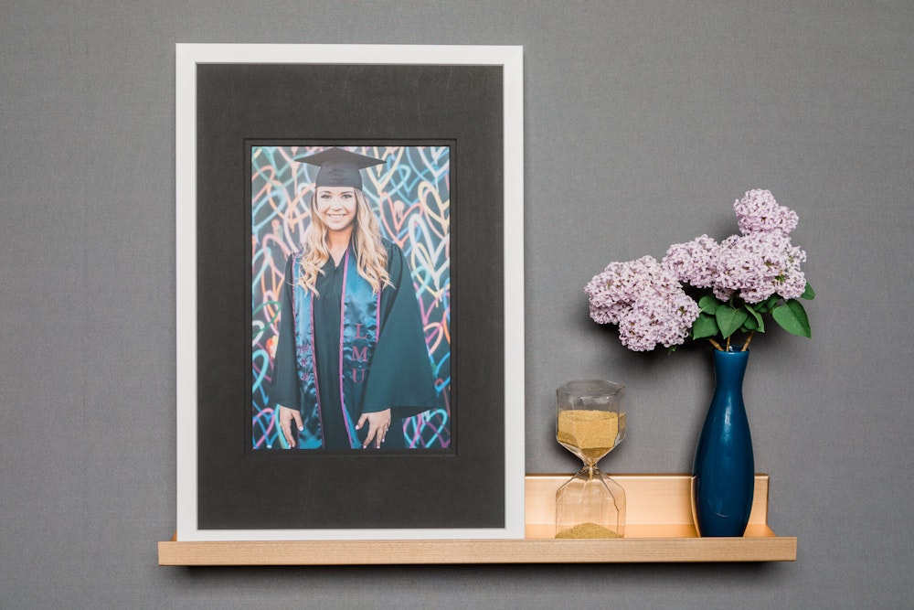 Colorful senior graduation portrait in cap and gown in silver Metal Framed Print with black mat on wall shelf